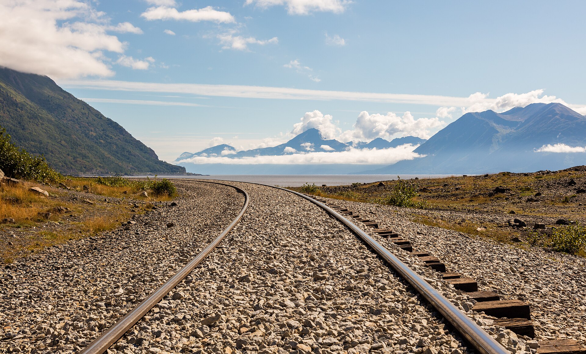 Railroad tracks curving along Turnagain Arm beneath mountains near Anchorage, Alaska